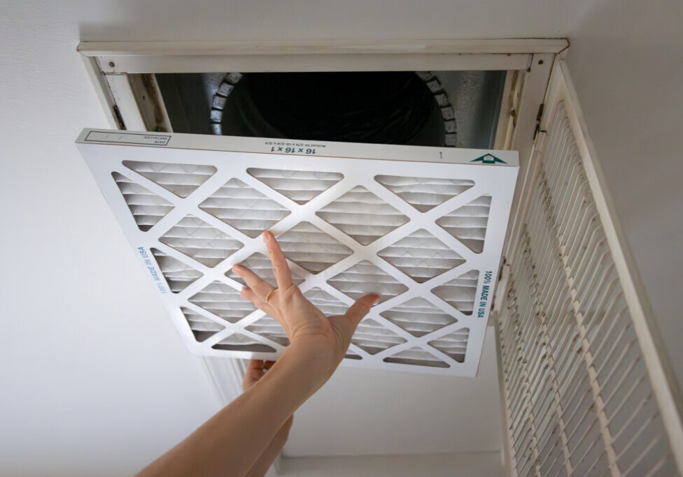 Adult white homeowner installing a new air filter in an intake vent in a home ceiling.