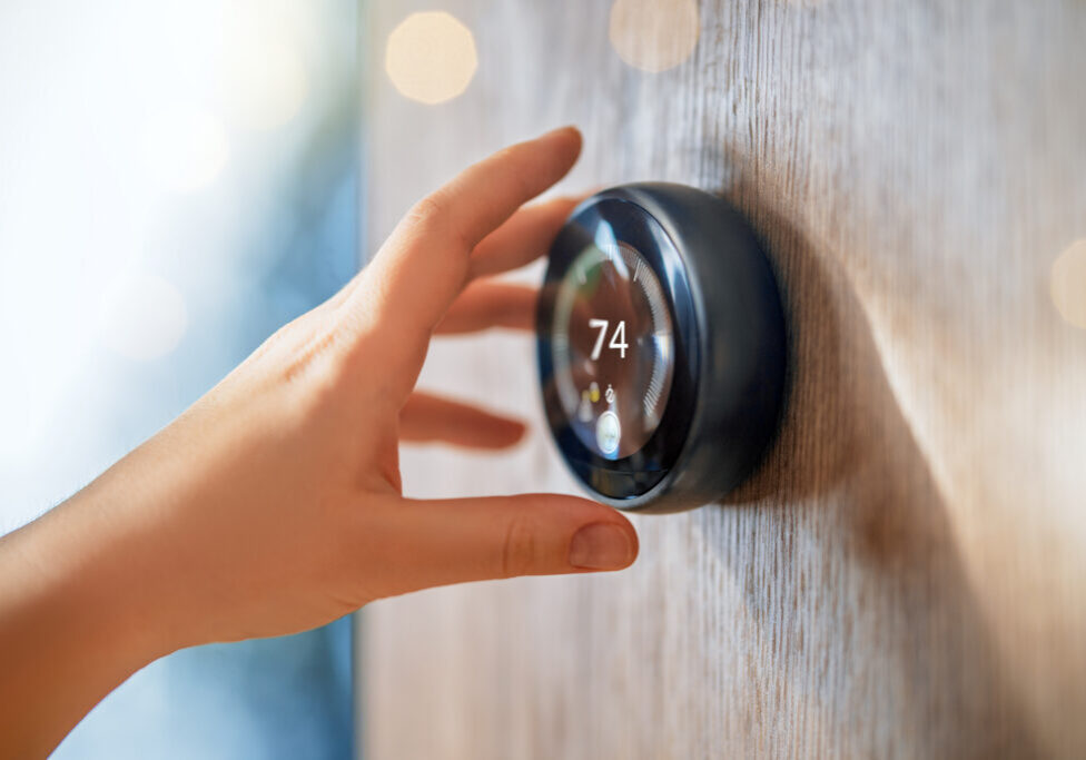 The hand reaching for the thermostat. Concept of smart home.