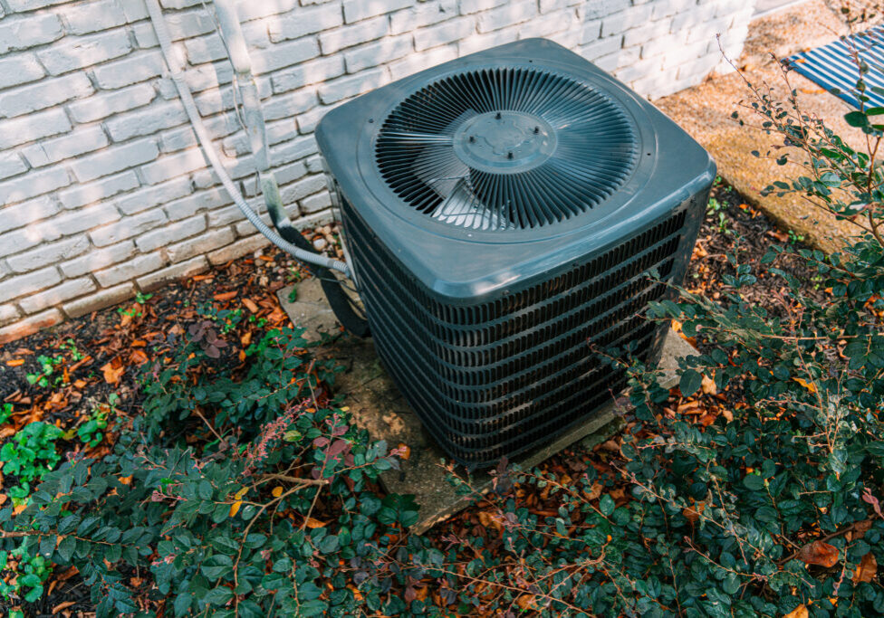 Air Conditioning Condenser Unit Mounted on a Concrete Slab outside of a Suburban Brick Home in Tennessee in Late Summer / Autumn Season Change